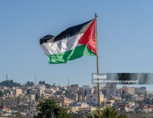 Palestinian Flag Flying High Over Jerusalem: A Symbol of Resilience "A large Palestinian flag waves proudly above the city of Jerusalem, symbolizing hope, resistance, and the enduring spirit of the Palestinian people. The ancient city's iconic structures, including the Dome of the Rock, can be seen in the background under a vibrant sky."