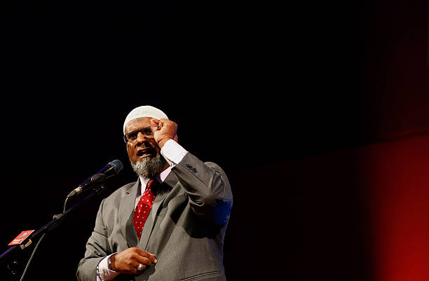 "Dr. Zakir Naik speaking into a microphone during a lecture, engaging the audience with his message."