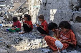 Palestinian school children sit amidst rubble, doing their homework in front of their destroyed school building in Gaza, showing resilience and commitment to education despite war.
